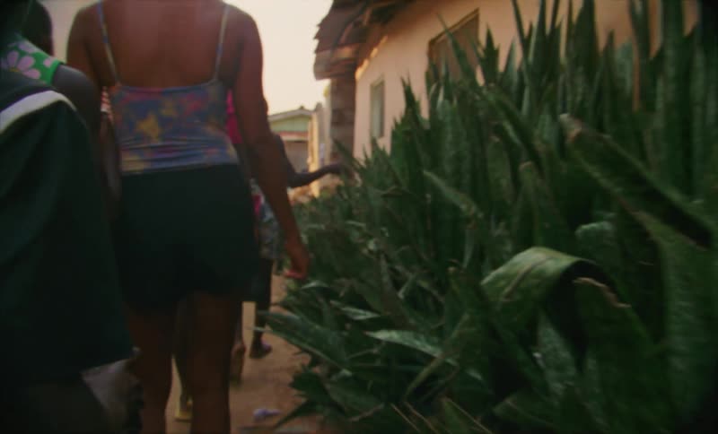 Family touch the leaves of plants growing on the side of a house in a third world country alley