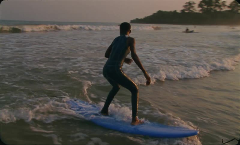 A boy is surfing on ocean water at dusk