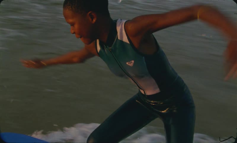 A child riding on a surfboard on his knees while he tries to stand up near the shore