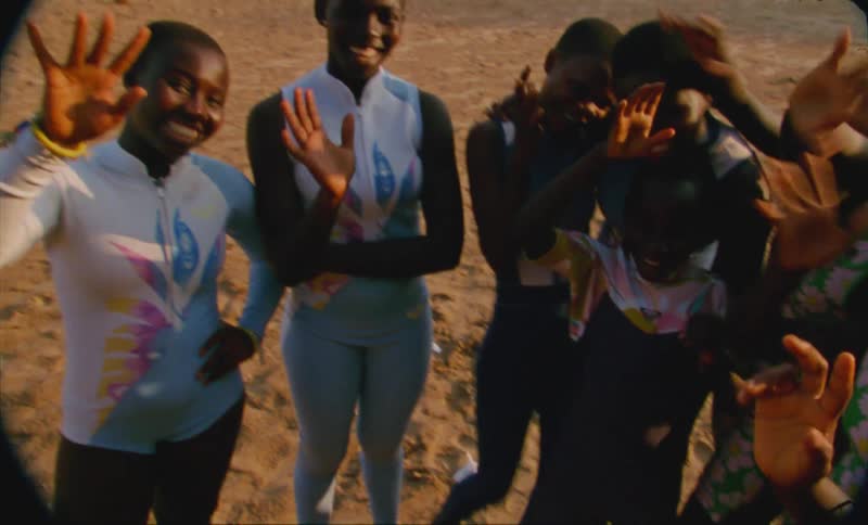A group of girls smiling and waving at camera on the beach