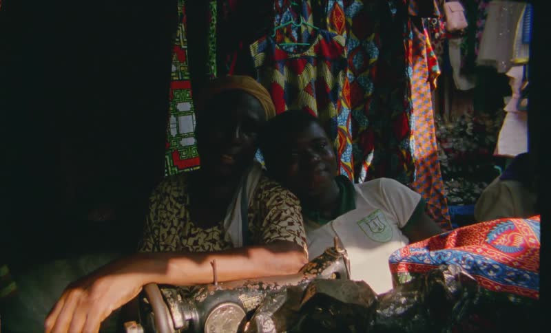 A mother and son sitting close together at a tailor shop with a sewing machine and garments