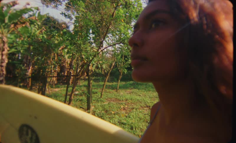 Young woman carrying a surfboard through a field in the tropics