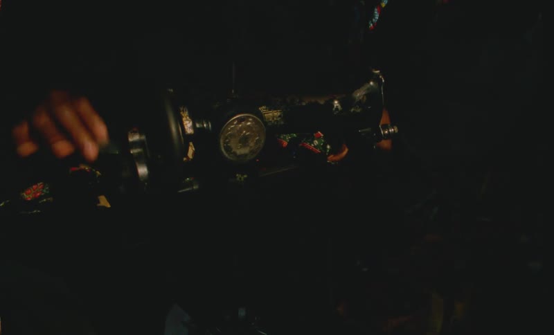 Person cranks handle to manually operate sewing machine in dark area