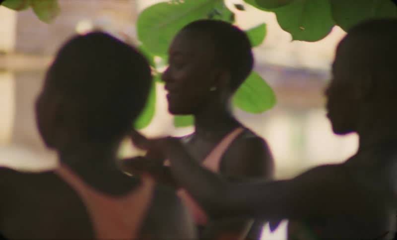 Three teenage girls wearing bathing suits and sundresses and dancing together in a community gathering