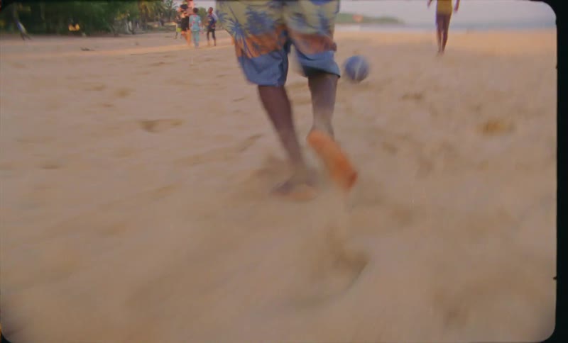 Speed up footage of boys playing soccer on a beach caught on vintage film