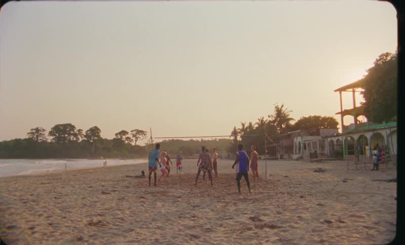 A group of children and teens playing volleyball on the sand at the beach during the day