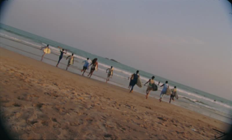 Group of happy friends running to the ocean carrying surfboards caught on vintage film