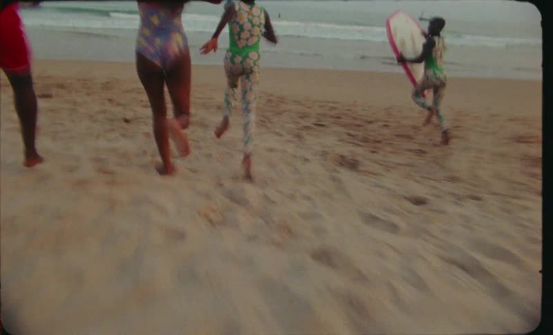 A group of young black girls run down a beach toward the ocean