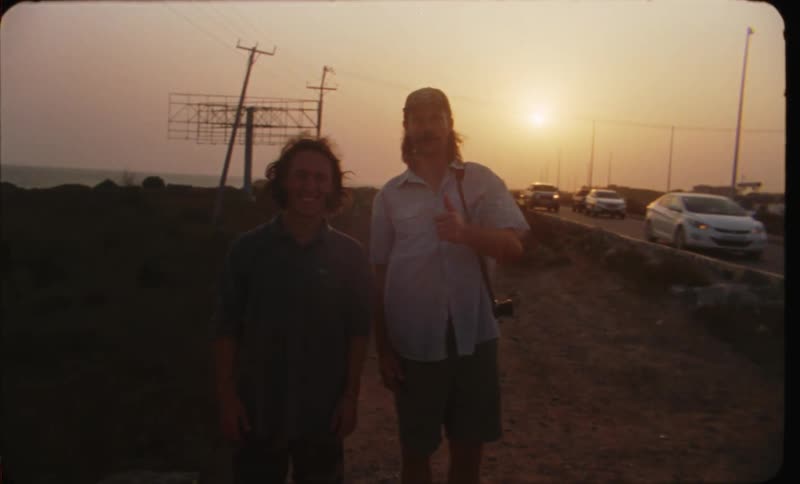 Two men are standing outside as cars are driving by