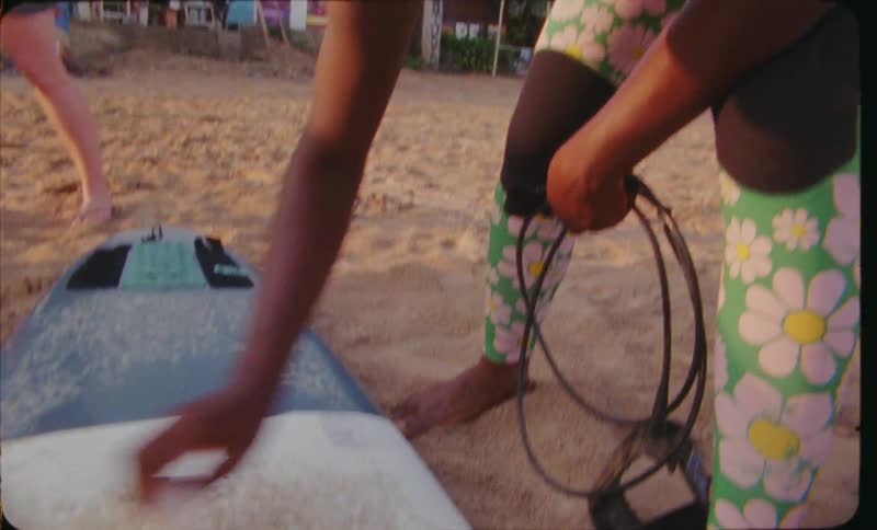Close up of a woman waxing the surface of a surfboard at the beach