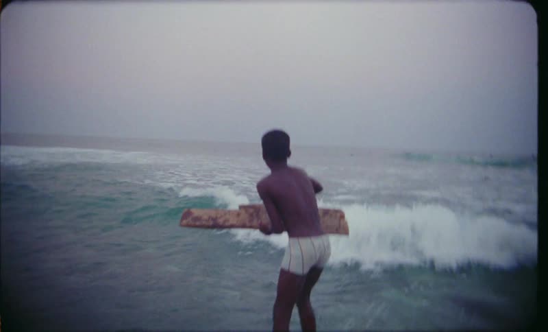 Speed up footage of a boy holding a plank jumping on a wave in shallow water caught on vintage film