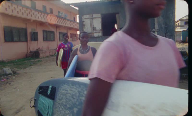 A group of young people are carrying their surfboards and smiling on a sunny day
