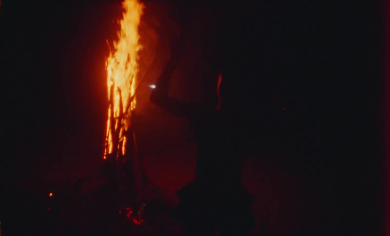A male is dancing outdoors next to a fire at night