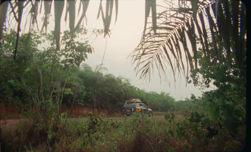 A car traveling on a dirt road with dense forests on either side and a person walking down the road