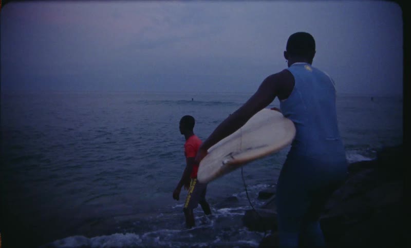 Man helps woman get surfboard then turns to watch other surfers approaching shore