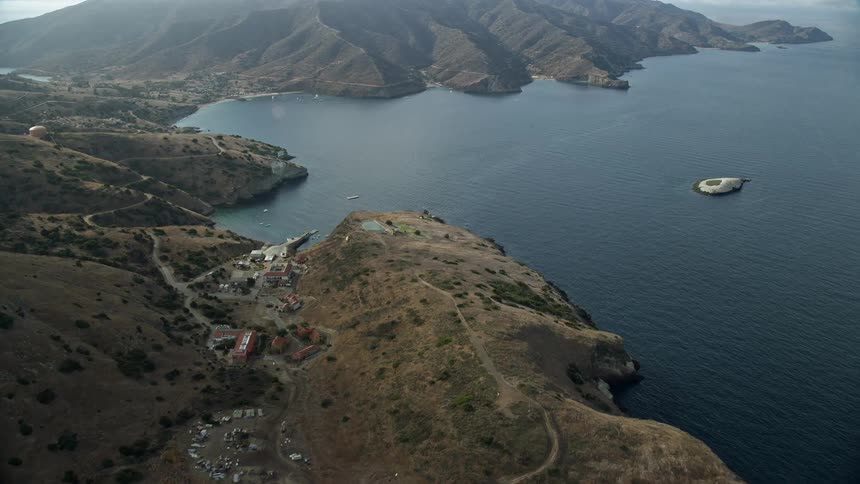 Flying over coastal cliffs and approaching the USC Wrigley Marine Science Center in Two Harbors Santa Catalina Island California on a partly cloudy day
