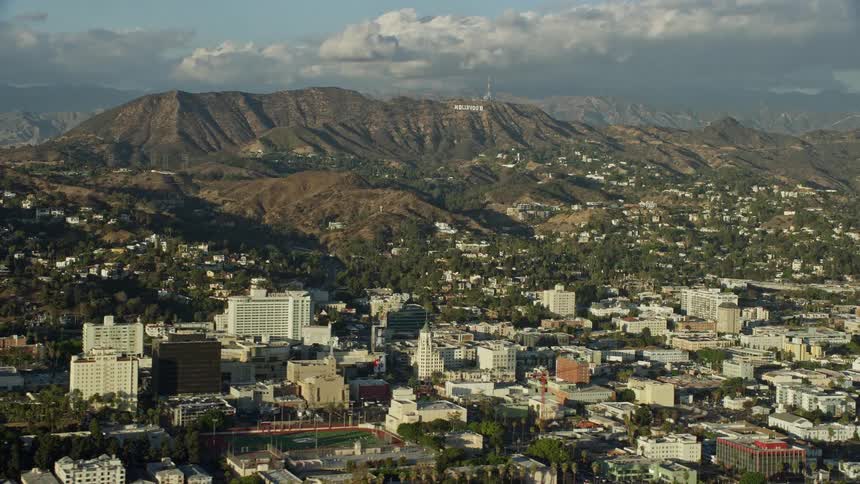 Aerial footage of the iconic Hollywood Sign and office buildings in Hollywood California with a sunny view of the city during the day time