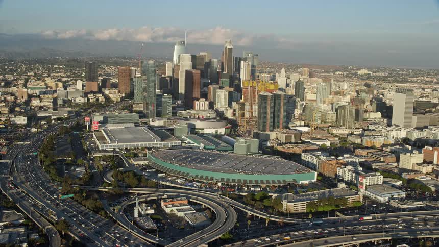 Aerial view of Downtown Los Angeles and its high-rise towers and skyscrapers in the daytime from the 10 and 110 interchange during a partly cloudy day with heavy traffic