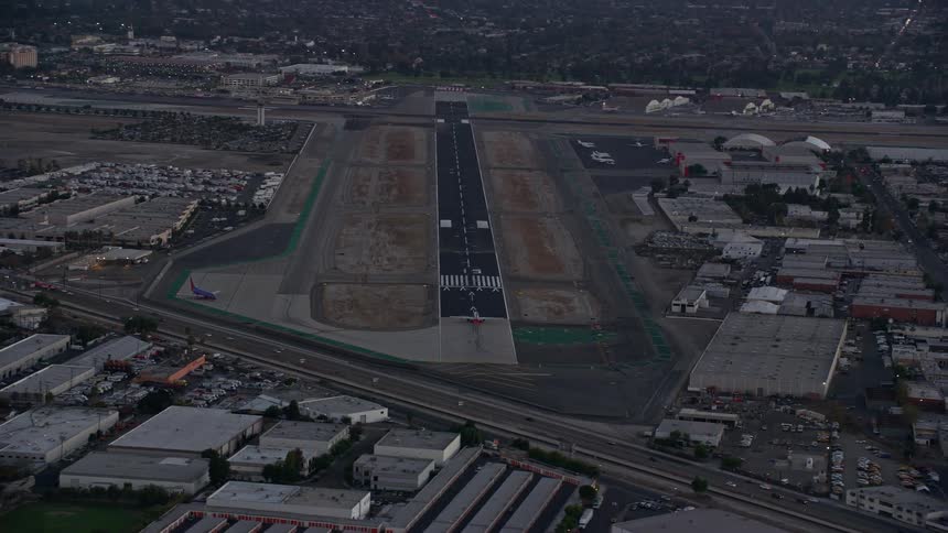 A commercial airplane takes off on the runway at Burbank Airport just as the sun is setting during a summer evening in California