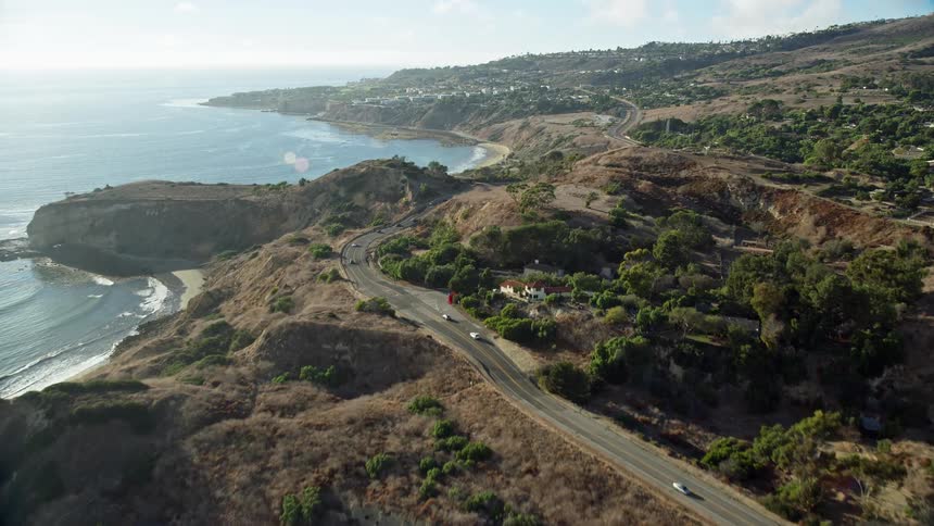 An aerial clip flying over an empty beach and approaching Palos Verdes Drive offering a side view of the coastal cliffs and shores of Rancho Palos Verdes in California during a partly cloudy day