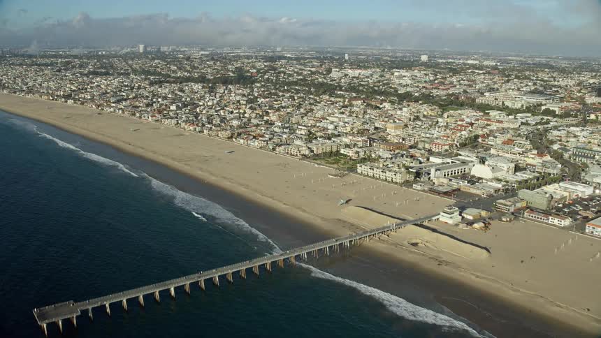 An aerial view of Hermosa Beach California featuring the city beach and pier during a partly cloudy day in spring or summer