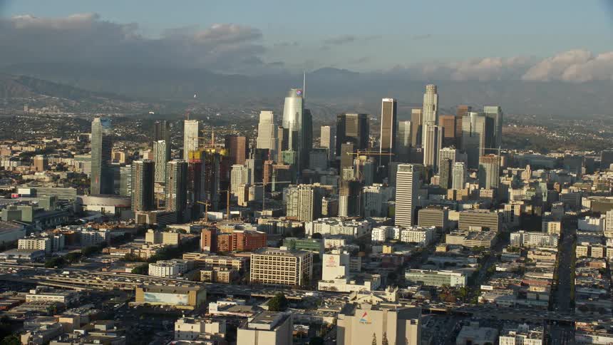 A breathtaking aerial view of Downtown Los Angeles seen from I-10 during daytime with partly cloudy skies and featuring high rises towers skyscrapers and supertalls in the background