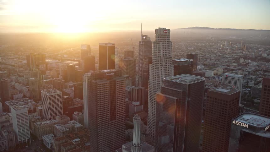 An awe-inspiring aerial stock footage of US Bank Tower orbiting at sunset in Downtown Los Angeles with the skyline of hazy tall office buildings and skyscrapers visible at dusk
