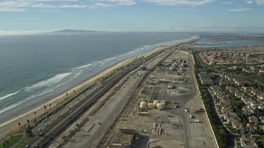 An aerial clip featuring residential areas around industrial sites and a beachfront along with PCH and highways in Huntington Beach California