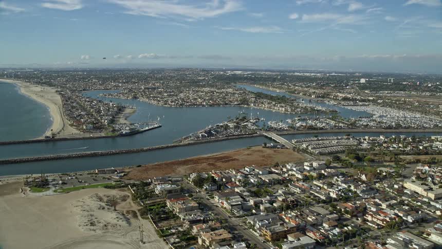 Aerial footage captures the scenic coastal neighborhoods around Alamitos Bay and an inlet in Long Beach featuring beach houses water bodies and partly cloudy skies in Southern California