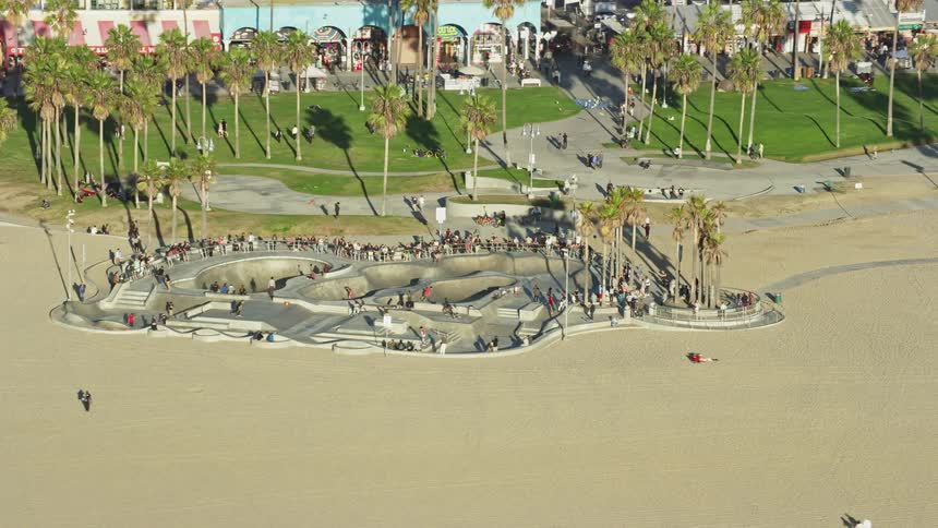 An aerial footage of Venice Skate Park on Venice Beach in California on a sunny day with people skateboarding and sunbathing