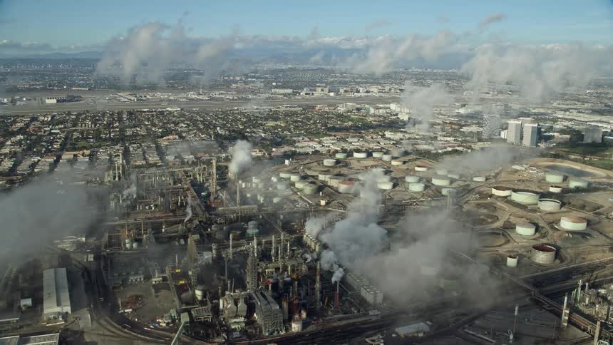 An epic shot revealing the Chevron oil refinery in El Segundo CA as aerial footage flies over low level clouds in partly cloudy skies during the day