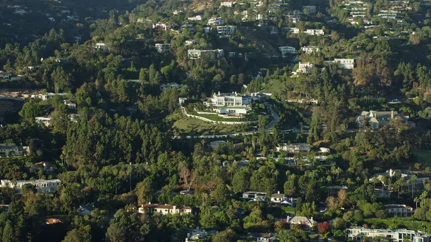 A stunning aerial view of a large hillside mansion with manicured grounds in sunny Beverly Hills California