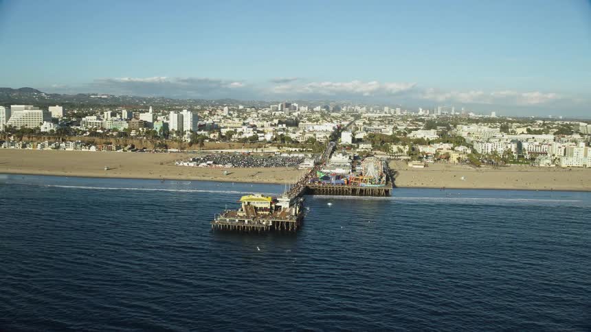 An aerial view of Santa Monica Pier in southern California showcasing the historic landmark and the popular beachgoers enjoying the sunshine during the summer