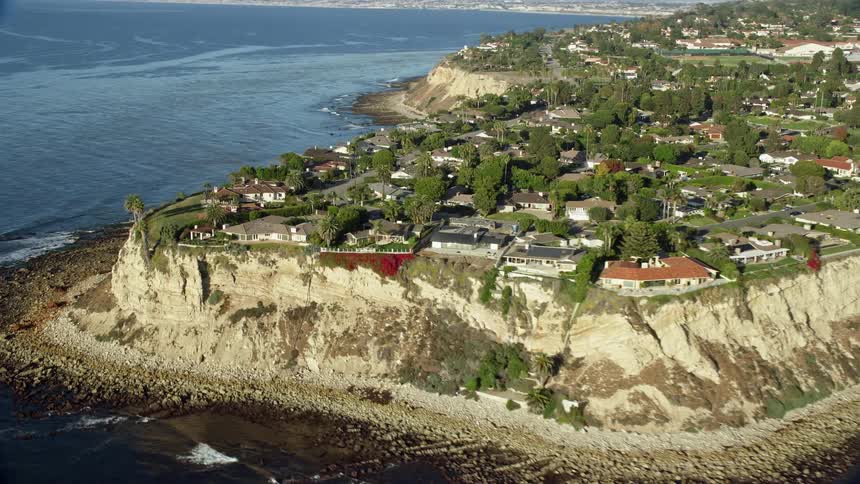 Aerial footage of mansions on clifftops in Palos Verdes Estates California overlooking the ocean on a partly cloudy day during spring or summer