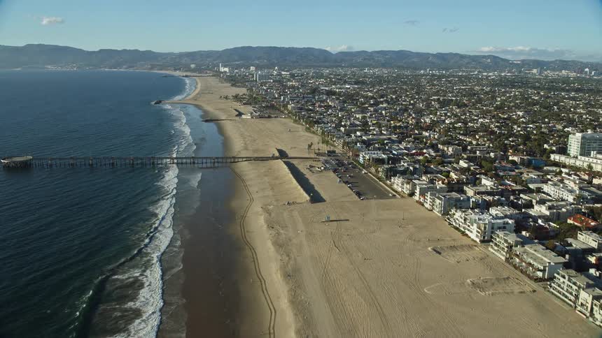 Fly over the empty beach and seaside residences towards the Venice Fishing Pier in Southern California during summer