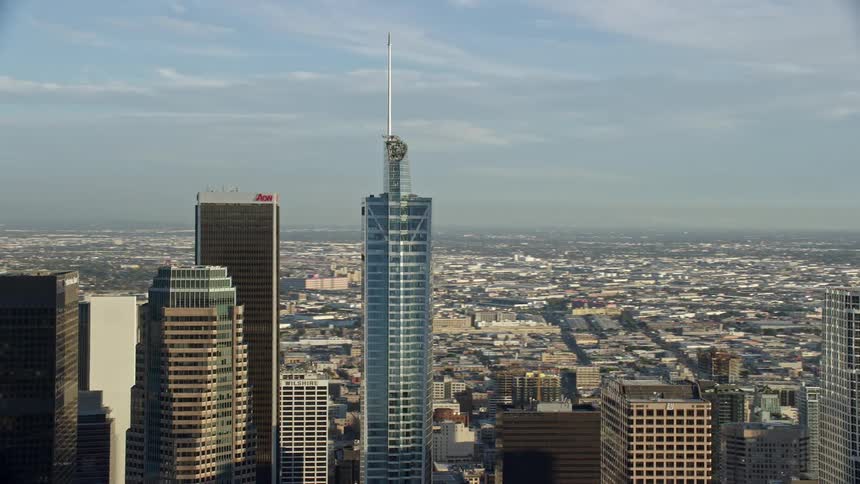 Flying over the Wilshire Grand Center skyscraper in Downtown LA during a partly cloudy day showcasing the citys towering modern buildings and supertalls