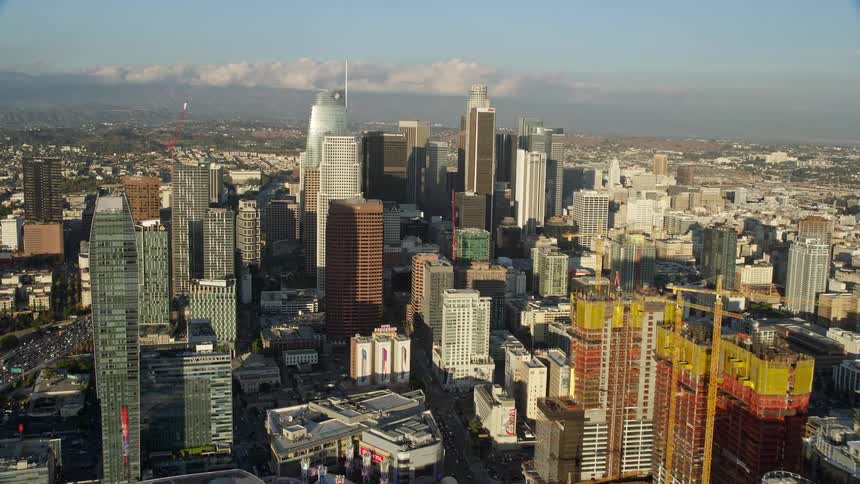 Aerial footage flies over Wilshire Grand Center and Aon Center to approach US Bank Tower in downtown Los Angeles California on a partly cloudy day showcasing the citys glass high-rises and supertalls