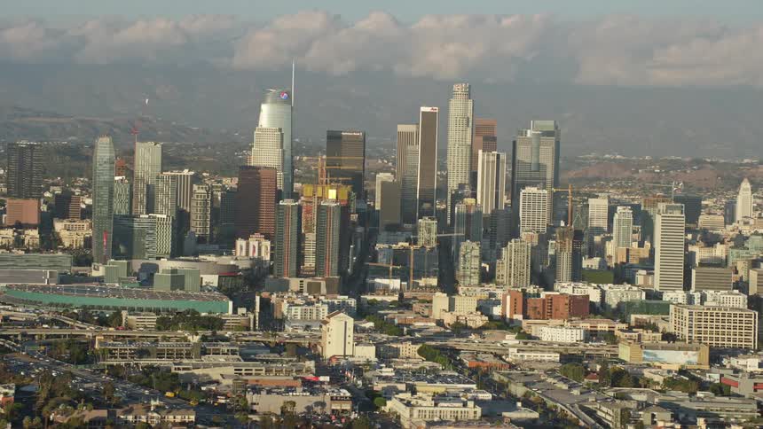 A breathtaking aerial view of Downtown Los Angeles impressive skyline featuring multiple tall skyscrapers against a partly cloudy sky in the midst of a sunny Summer day