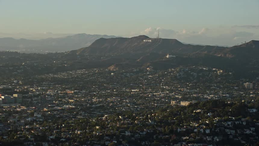 Aerial footage of the iconic Hollywood Sign and Griffith Observatory viewed from Silver Lake during a partly cloudy day in California