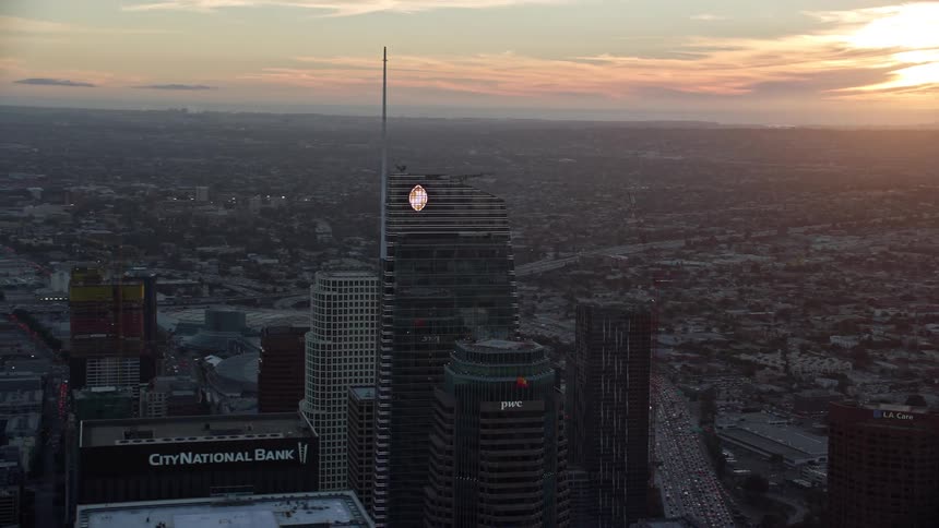 Aerial footage of Wilshire Grand Center and US Bank Tower during sunset in Downtown LA showcasing the towering modern glass buildings against the partly cloudy sky