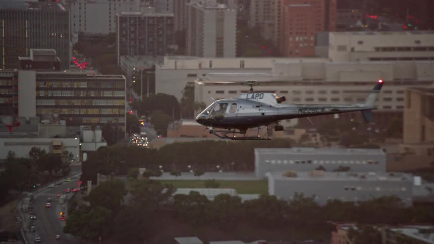 An LAPD helicopter flies by Downtown Los Angeles California during twilight in a aerial stock footage