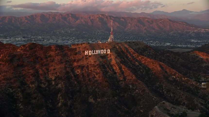 An aerial shot of the iconic Hollywood Sign at twilight in Los Angeles California showing the sign on a cliff against the backdrop of partly cloudy skies during the summer
