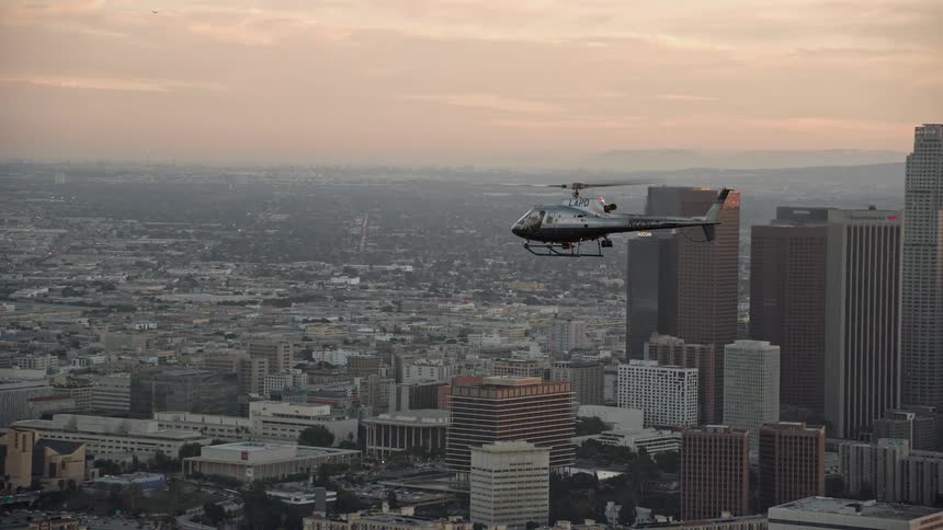 An LAPD helicopter flies over the Downtown Los Angeles skyline at twilight captured in aerial stock footage