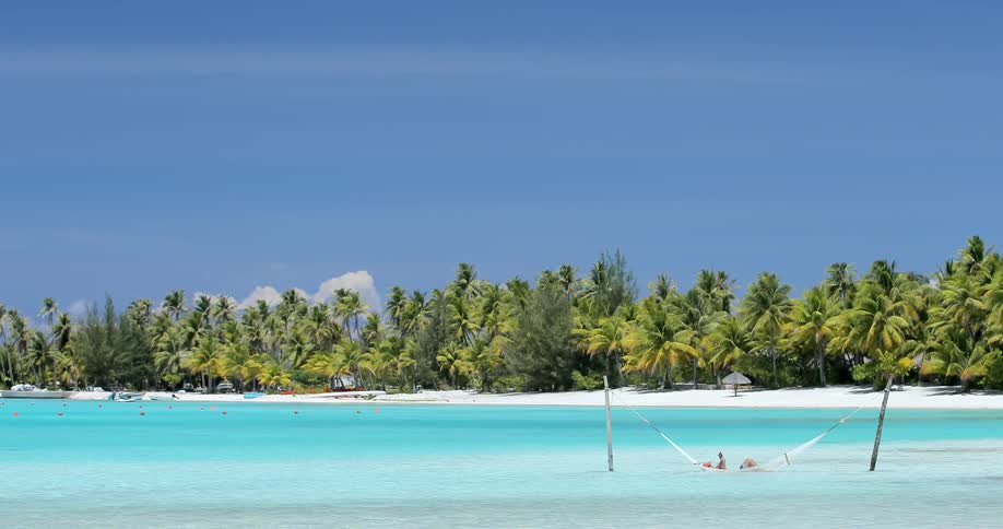 People sitting in a hammock in the water near an island beach
