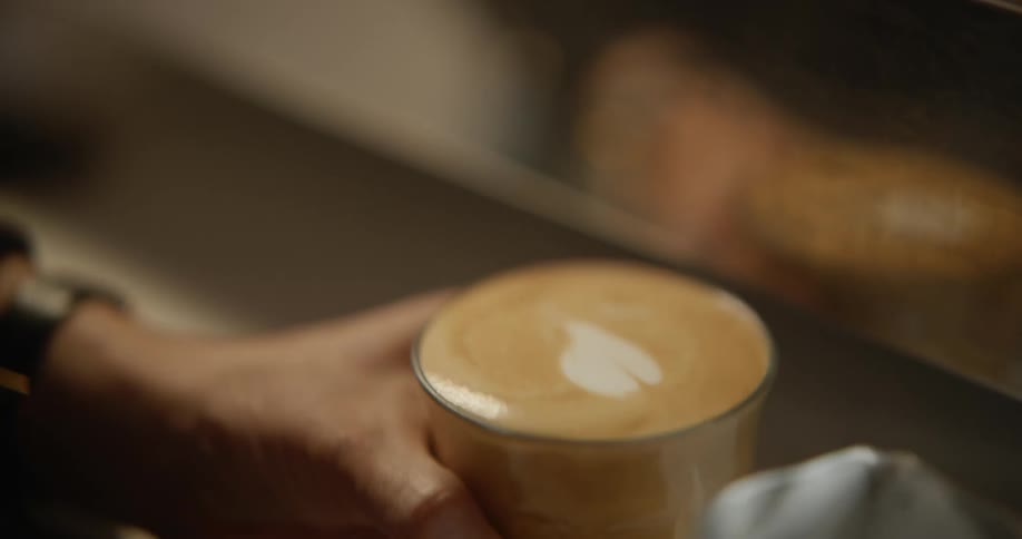Close up of a barista adding milk to coffee, creating a heart shape on the surface
