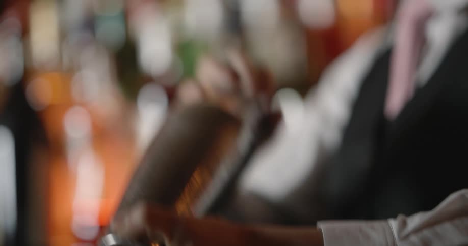 A bartender mixes a cocktail in a metal shaker