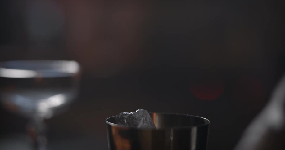A bartender puts ice into a cocktail mixer