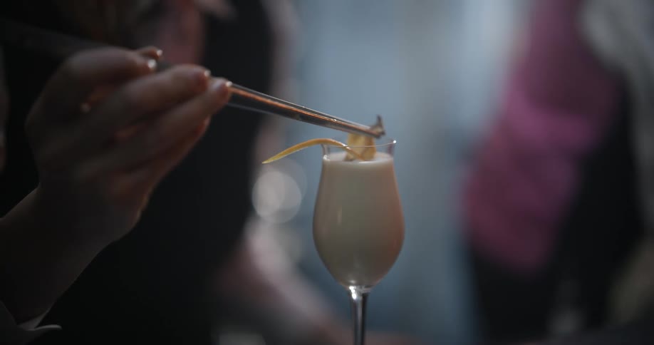 A bartender finishes off a cocktail with  a piece of fruit peel