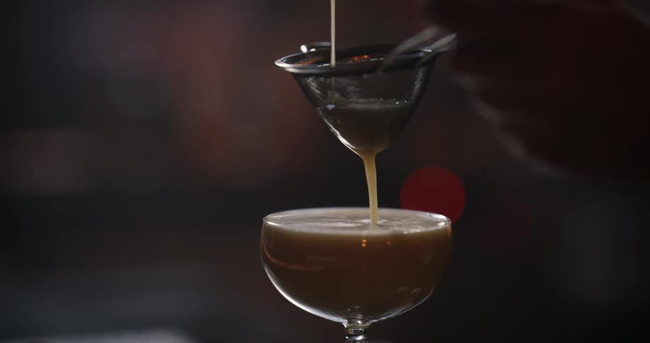 A bartender pours a cocktail through a strainer and into the glass