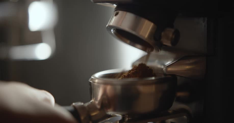 A close up of a portafilter being filled with ground coffee from a grinder.